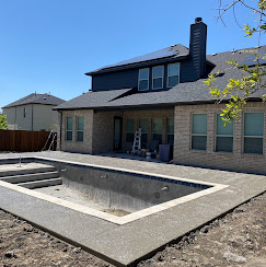 Freshly formed concrete pool shell behind a two-story brick home